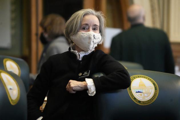 picture of CO Rep Judy Amabile wearing a black sweater and wearing a face mask with her arm on a green chair in the Colorado State Capitol