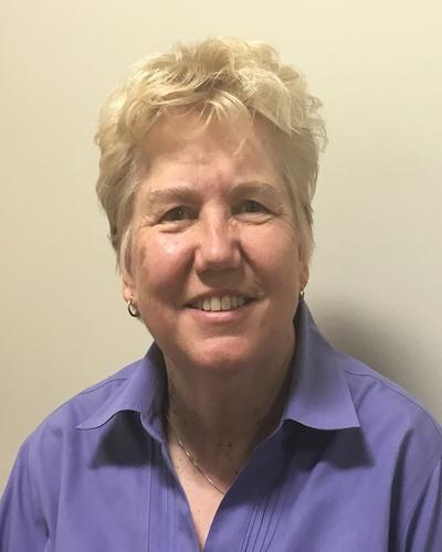 white older woman with light blonde hair with a periwinkle blue collared shirt.  She's smiling at the camera.