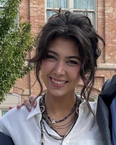 picture of Lynnie Lucas smiling and wearing a white shirt and necklaces in front of a red and cream bricked building at Denver University