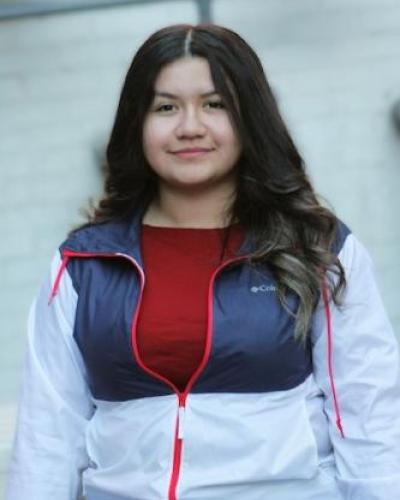 Latina woman with long dark hair wearing a red shirt with a white and blue jacked over 